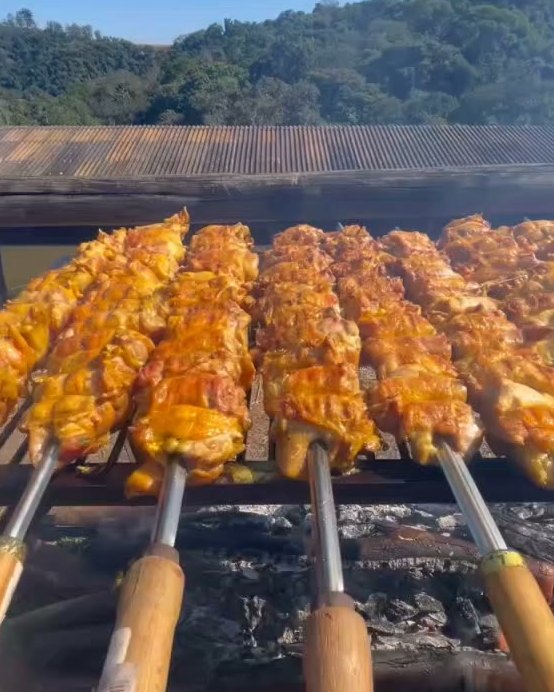 Espetos de carne dourando sobre a brasa ao ar livre