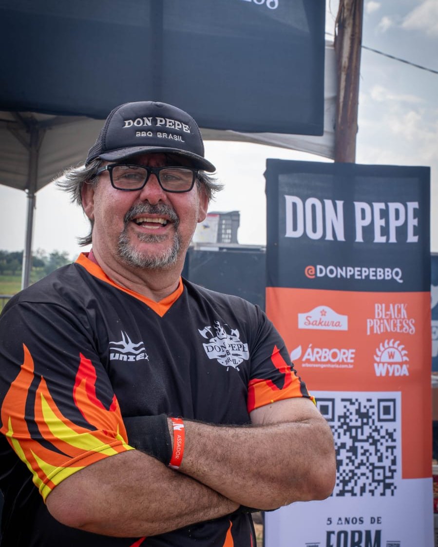 Don Pepe de braços cruzados, com boné e uniforme de chamas, no estande Don Pepe do Farm Festival