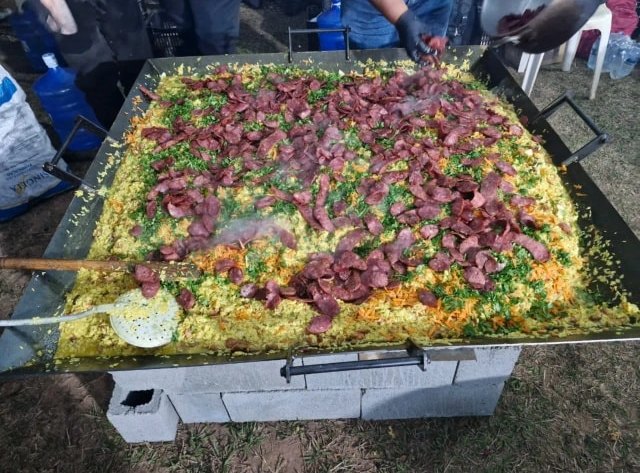 Tacho enorme de arroz com linguiça e cheiro-verde, preparado ao ar livre